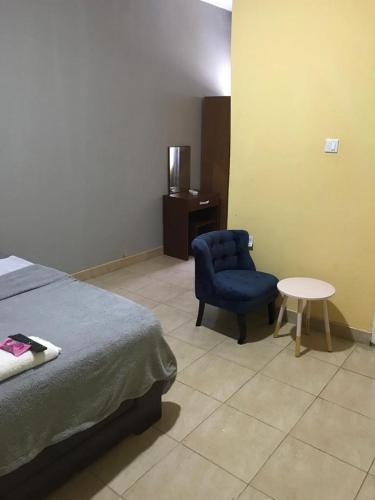 een slaapkamer met een bed en een blauwe stoel en een tafel bij Danson Lodge Guest House in Pokuase