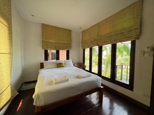 a bedroom with a large bed with windows at เฮือนริมน่าน Huen Rim Nan in Nan