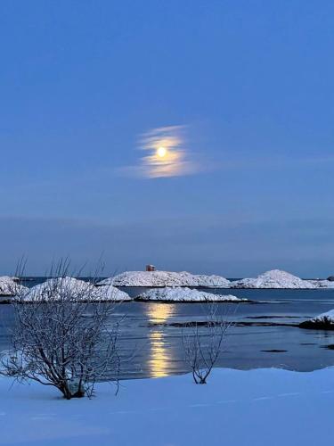 a moon flying over a body of water with snow at Apartment Utsikten in Andenes