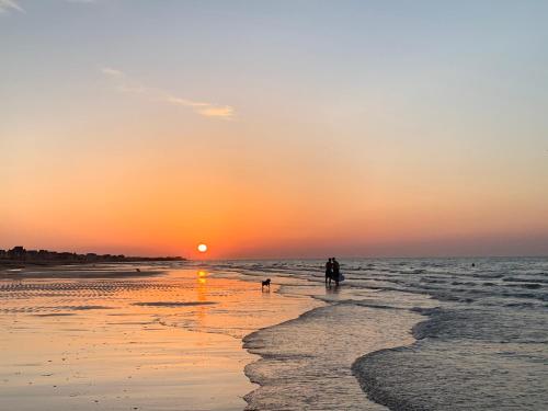 a person and a dog walking on the beach at sunset at A Casa Mia Plage in Hermanville-sur-Mer