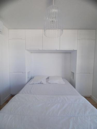 a white bedroom with a bed and a chandelier at Fenestrelle By LGM une chambre, climatisation, wifi in La Grande-Motte