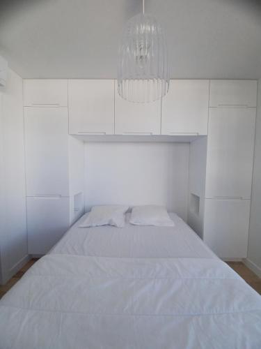 a white bedroom with a bed and a chandelier at Fenestrelle By LGM 57m2 clim, wifi, ménage inclus in La Grande-Motte