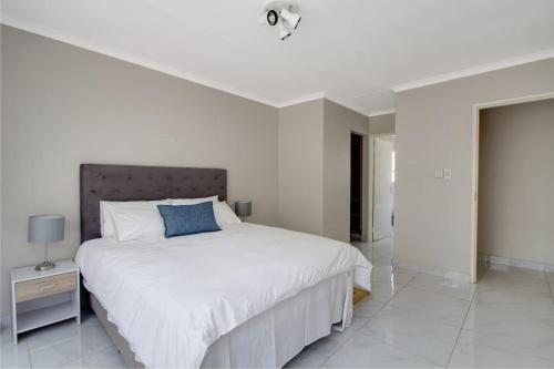 a white bedroom with a large bed with a blue pillow at The Cycad. 4-Bed Home next to Clearwater Mall in Roodepoort