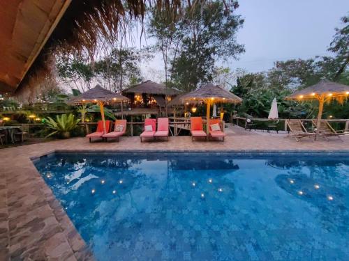una piscina con sillas, mesas y sombrillas en Jungle Moon Homestay จังเกิ้ลมูน โฮมสเตย์ บางเสร่ en Sattahip