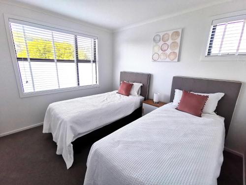 um quarto com 2 camas com lençóis brancos e almofadas vermelhas em Nelson City Town House 10 minute walk to town em Nelson