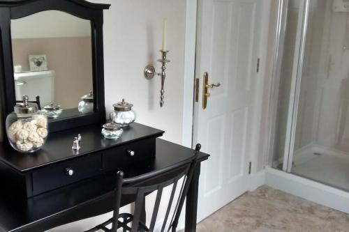 een zwarte dressoir met een spiegel en een zwarte stoel bij 7 Burnside House in Kilmorack