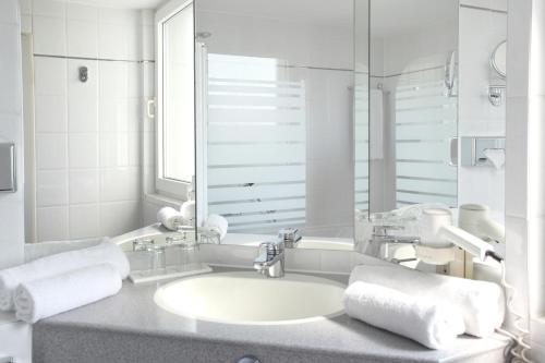 a white bathroom with a sink and a mirror at ABACUS Tierpark Hotel in Berlin
