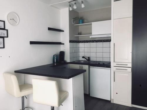 - une cuisine blanche avec un comptoir noir et des chaises blanches dans l'établissement Cozy'Cocoon, à Brest