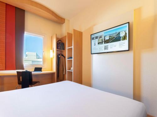 マドリードにあるIbis Madrid Calle Alcaláの壁にテレビとベッドが備わる客室です。