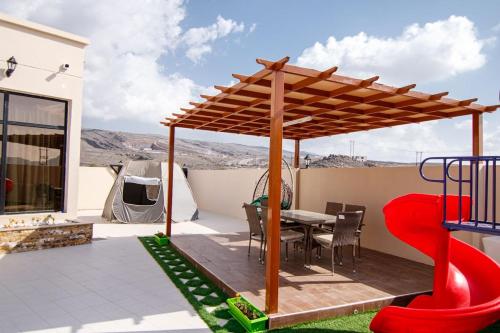 a patio with a table and a wooden pergola at Estrahet Al Haitham in Al Qal‘ah