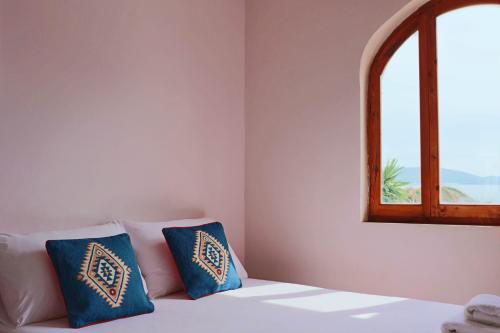 a bed with two blue pillows and a window at Hotel Villa Margarit in Sarandë