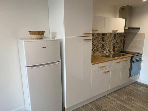 La cuisine blanche est équipée d'un réfrigérateur et d'un évier. dans l'établissement Studio rénové 200 m de la plage avec parking privé, au Cap d'Agde
