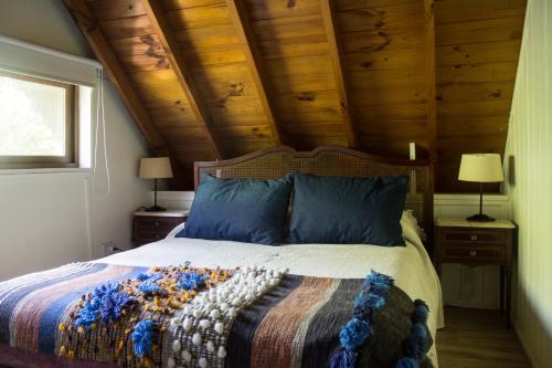 1 dormitorio con cama con almohadas azules y techos de madera en Pinamar Bosque en Pinamar
