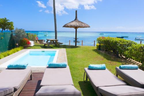 a swimming pool with two chaise lounges next to the ocean at Caro's Beachfront in Trou aux Biches