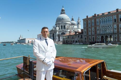 a man in a white suit standing in front of a boat at The Gritti Palace, a Luxury Collection Hotel, Venice in Venice