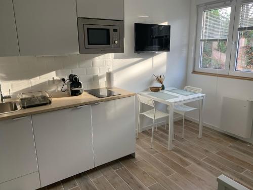 une cuisine avec des armoires blanches, une table et un micro-ondes dans l'établissement Charmante studette au cœur du Plessis Robinson, au Plessis-Robinson
