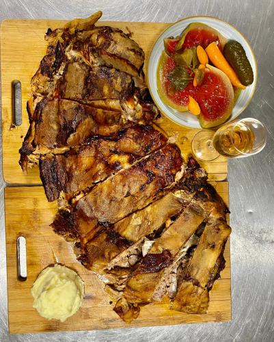 a wooden cutting board with meat and a bowl of fruit at Pensiunea Știuca Șchioapă in Băltenii de Sus