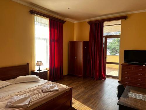 SWEET HOME HOTEL Meghri في Meghri: غرفة نوم بسرير مع ستائر حمراء وتلفزيون