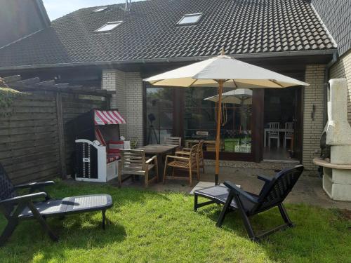 eine Terrasse mit Tisch, Stühlen und Sonnenschirm in der Unterkunft Ferienhaus Kleine Robbe in Friedrichskoog
