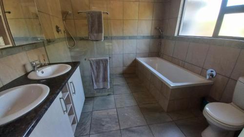 La salle de bains est pourvue de 2 lavabos, d'une baignoire et de toilettes. dans l'établissement Oribi Gorge Villa, à Glendale
