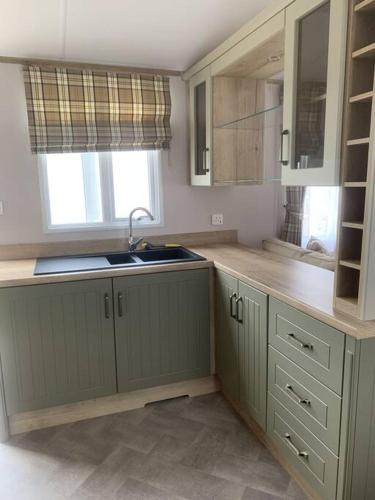 cocina con armarios verdes, fregadero y ventana en Grasmere Lodge Unit 31 en Carlisle