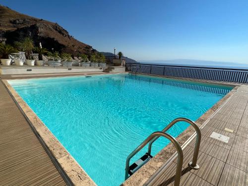 una gran piscina azul con una terraza de madera y el océano en La Maison De Marie en Taormina