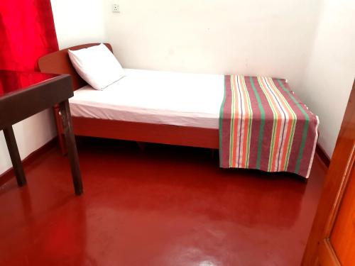 a small bed in a room with a red floor at Nallur Holidays Inn in Jaffna