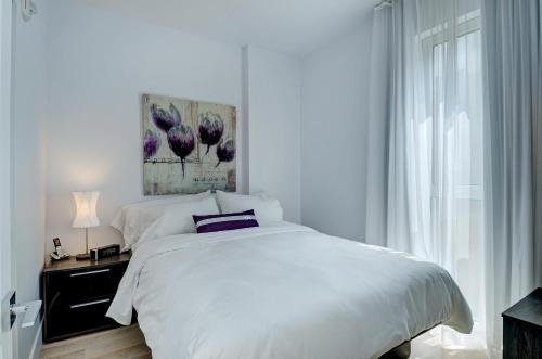 a white bedroom with a bed and a window at Les Immeubles Charlevoix - Le 760-507 in Quebec City