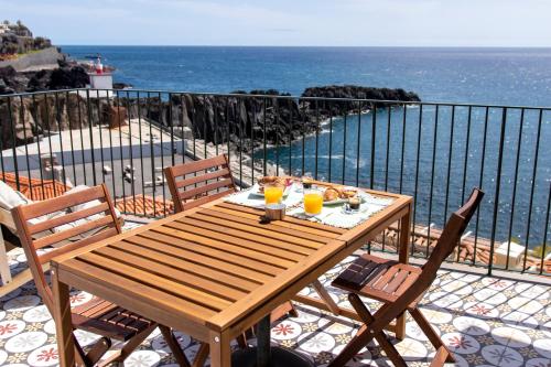 a wooden table and chairs on a balcony with the ocean at Casa do Ilhéu - House of Ilhéu - Câmara de Lobos in Câmara de Lobos