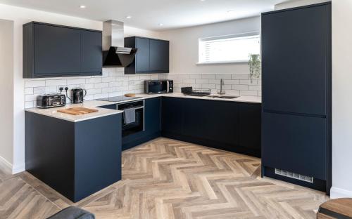 a kitchen with black cabinets and a wooden floor at Modern new build, Close to the beach and town in Bude