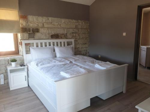 Una cama blanca en un dormitorio con una pared de piedra. en Ракшиева Къща en Glavatartsi