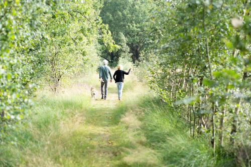 a man and a woman walking a dog on a trail at Ieberen lodge in Schoonloo