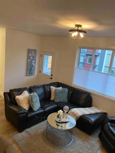 a living room with a black leather couch and a table at Adorable 1 Bedroom Suite- a skip to Galloping Goose in Victoria