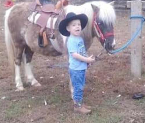 Ein Junge mit einem Cowboyhut, der neben einem Pferd steht. in der Unterkunft Goin' Bonanza Glamping Ranch in Hardy
