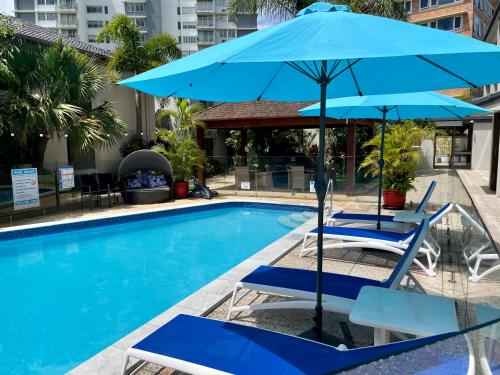 a pool with two chairs and a blue umbrella at Burleigh Palms Holiday Apartments in Gold Coast