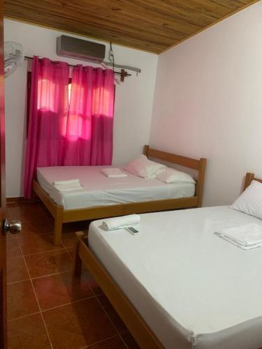 Habitación con 2 camas y ventana con cortinas rosas. en HOSTAL ESPERANZA en Palomino