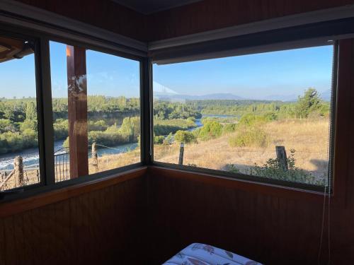 a room with three windows with a view of a river at Cabañas Trialye in Quilaco