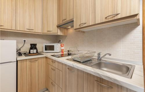 een keuken met houten kasten, een wastafel en een magnetron bij Cozy Apartment In Crikvenica With Kitchen in Crikvenica