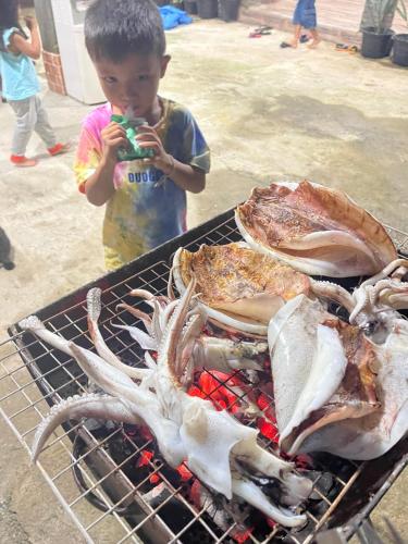 a boy standing next to a grill with a large lobster at เกาะลิบงซันไรส์ โฮมสเตย์ Koh libong sunrise Homestay in Ko Libong
