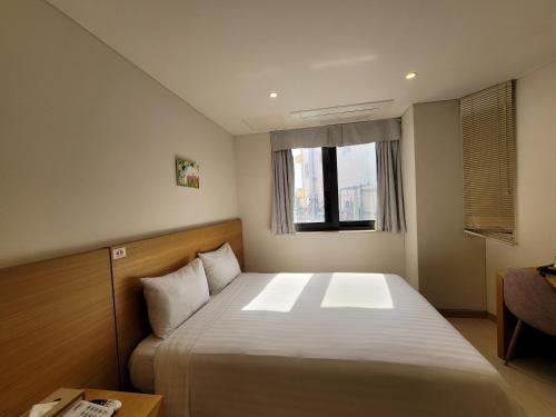 a small bedroom with a bed and a window at BK Hotel Jeju in Seogwipo