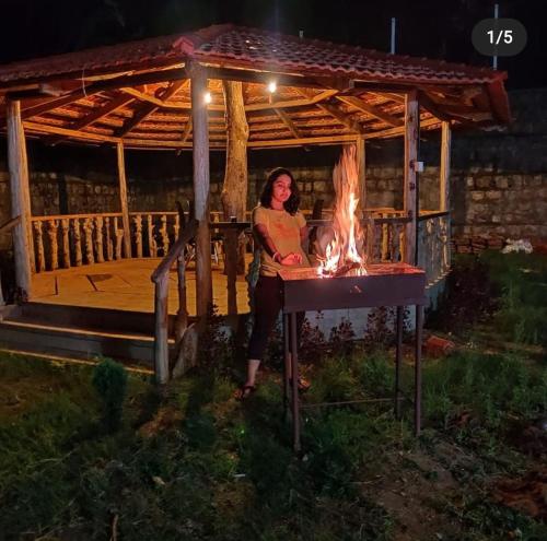 a woman standing in front of a fire in a gazebo at Little bungalow Holiday Home, Coorg in Somvārpet