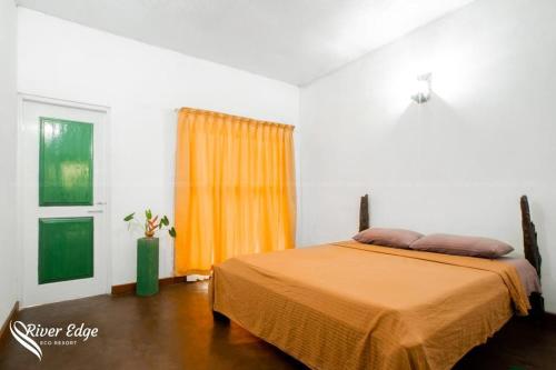 - une chambre avec un lit doté d'un couvre-lit orange et d'une fenêtre dans l'établissement River Edge Eco Resort, à Kitulgala