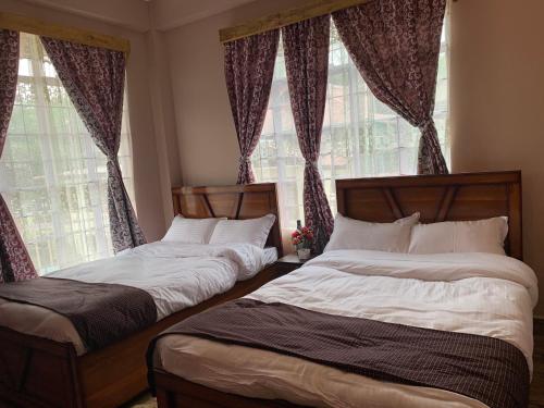 2 Betten in einem Zimmer mit 2 Fenstern in der Unterkunft Tariang's Enclave Homestay in Shillong