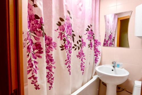 een badkamer met een wastafel en een douchegordijn met paarse bloemen bij В центре Павлодара светлая квартира in Pavlodar