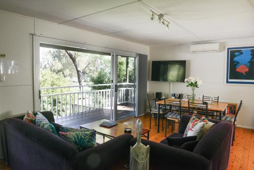 a living room with couches and a table and a balcony at Paradise Bungalow Waterfront in Sanctuary Point