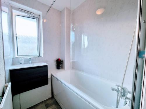 a white bathroom with a tub and a window at Lovely House with garden in London