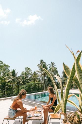 two women sitting on tables next to a swimming pool at Atrium Hiriketiya in Hiriketiya