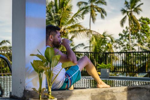 a man sitting on a ledge talking on a cell phone at Atrium Hiriketiya in Hiriketiya