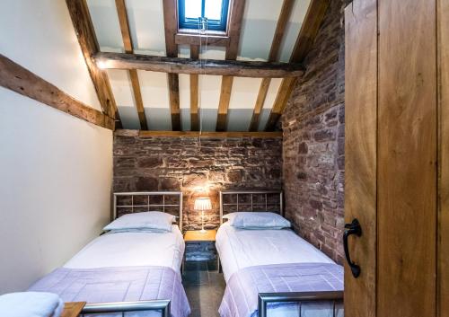 two beds in a room with a stone wall at Pomona Cottage at Old King Street Llama Farm in Ewyas Harold