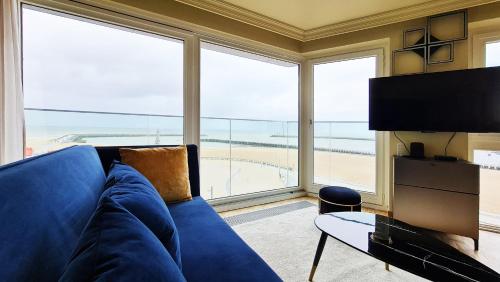 a living room with a blue couch and a large window at Maui - zeezichtappartement te Oostende in Ostend